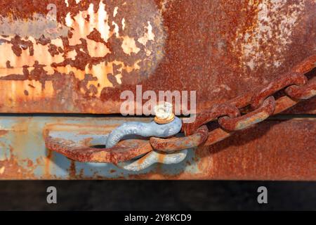 Photograph of an old D Bolt shackle connected to a rusty chain on a large brown and rusty metal storage container. Stock Photo