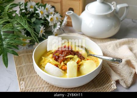 A bowl of “Lontong” or rice cake and coconut gravy with tumeric, chilli, and vegetables. Stock Photo