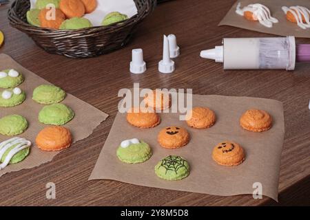 Process of making Halloween macarons. White icing in pastry syringe and cookie halves on kitchen table. Baking macarons at home close-up. Stock Photo