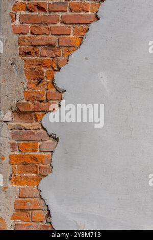 A red brick wall half covered with plaster. The wall is old and has many cracks. Stock Photo