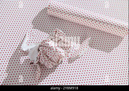 Crumpled red polka dot wrapping paper with a roll on a matching background, highlighting holiday or creative concepts. Stock Photo