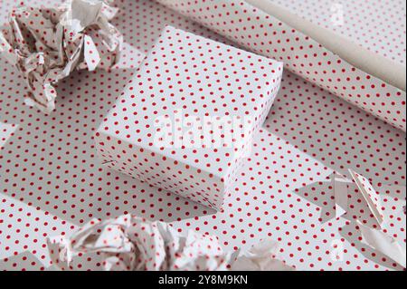 A beautifully wrapped gift box in white and red polka dot paper, surrounded by rolls and crumpled paper, suggesting a festive celebration or special o Stock Photo