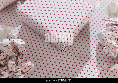 A beautifully wrapped gift in red polka dot paper amidst crumpled wrapping material, evoking a festive and cheerful atmosphere. Stock Photo
