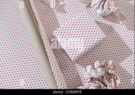 A wrapped present with red polka dots on white paper, surrounded by crumpled sheets, on a bright surface. Stock Photo