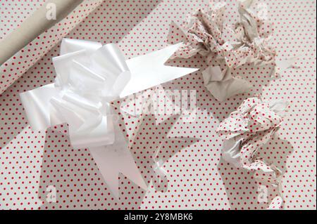 Close-up of festive gift preparation featuring a white bow on red polka dot paper, symbolizing celebration and creativity. Stock Photo