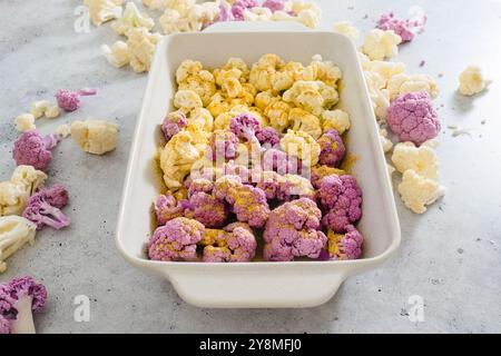 Cauliflower, white and purple, in baking pan with garlic seasoning, ready to be baked. Close-up view, grey stone background Stock Photo