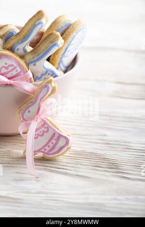 Pink clay bowl full of homemade Easter cookies in shape of bunny on white wooden kitchen table. Place for text Stock Photo