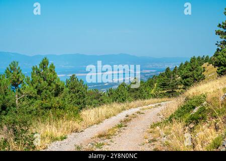 Unpaved road under blue sky through the hilly landscape of the Croatian Mountains. Stock Photo