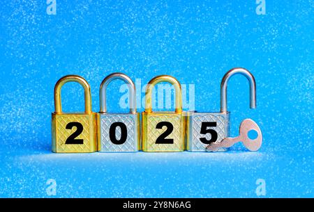 Row of padlocks showing the year 2025, accompanied by a key on a snowy blue background. One padlock is open. New beginnings and aspirations concept. Stock Photo