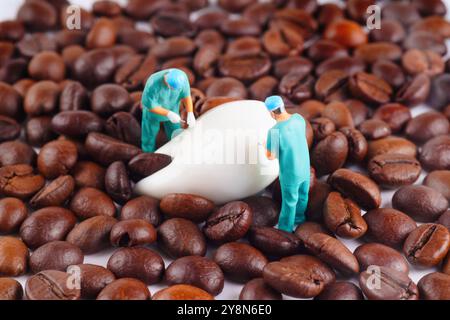 Miniature dentists performing dental procedures on a white tooth model amidst a backdrop of roasted coffee beans, representing dental care and coffee Stock Photo