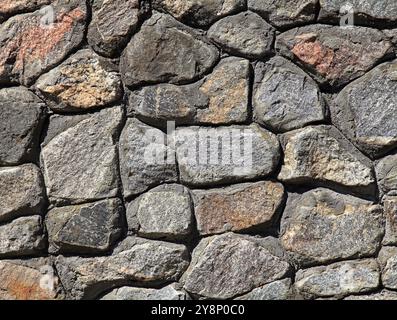 Granite wall, background. Surface of stone structure built of granite rocks (bricks). The wall texture of volcanic grey color. Fence backdrop Stock Photo