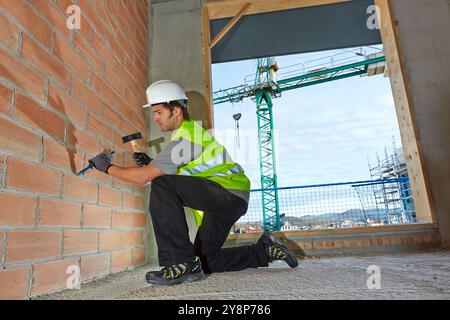 Mason by slashing the wall with hammer and chisel, Bricklayer with personal protective equipment, PPE, Apartment Building under construction, Donostia, San Sebastian, Gipuzkoa, Basque Country, Spain. Stock Photo