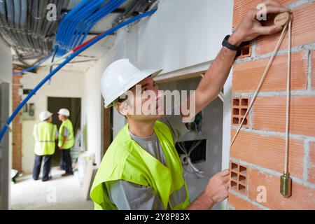 Worker with protective equipment, PPE, Checking and aligning vertical sections in brick wall, housing construction, Plumb line, Basque Country, Spain. Stock Photo