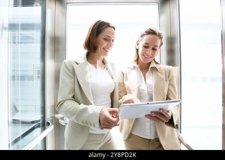 Two executives in elevator, using a digital tablet. Stock Photo