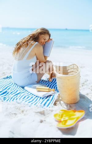 happy stylish woman on the ocean shore with straw bag, book and striped towel. Stock Photo