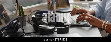 Website header shot of female hands typing on computer keyboard and headphones lying on working desk of software developer, office setup Stock Photo