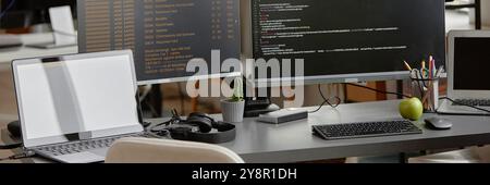 Website header shot of programmer desk setup with laptop and multiple computer screens displaying source code programming at office workplace Stock Photo