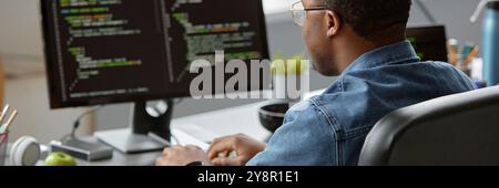Website header shot of African American male IT developer code programming on computer while sitting at desk in office, copy space Stock Photo