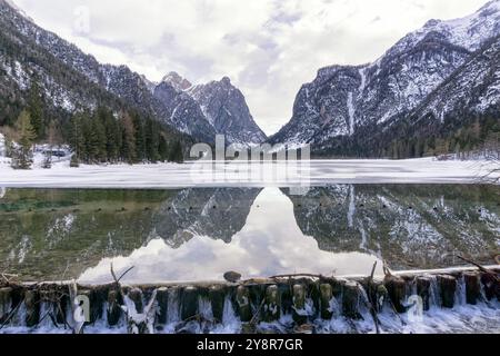 Winter mountain landscape at a snowy and partly frozen Lake Dobbiaco, Mountains reflected in the water, Cloudy sky. Province of Bolzano, Trentino Alto Stock Photo