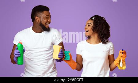 Cleaning Offer. Excited Black Couple With Household Tools Standing Over Pink Background Stock Photo
