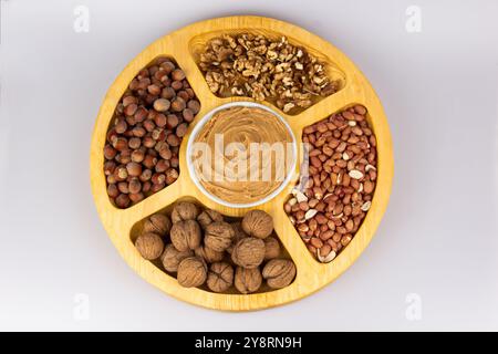 Creamy peanut butter, peanut butter in an open glass jar in the center of a peanut food background. Peanuts in shell, peeled peanuts on a white Stock Photo
