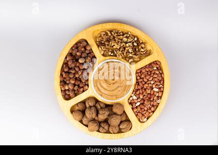 Creamy peanut butter, peanut butter in an open glass jar in the center of a peanut food background. Peanuts in shell, peeled peanuts on a white Stock Photo