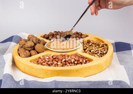 Creamy peanut butter, peanut butter in an open glass jar in the center of a peanut food background. Peanuts in shell, peeled peanuts on a white Stock Photo