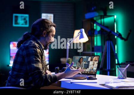 Young guy participating in an online meeting with a group of people seen on laptop screen. They are communicating, comparing notes, and actively involved in video conference from different locations. Stock Photo