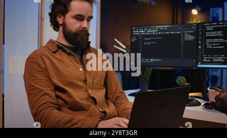 Freelancing computer scientist starting work in personal office at home, taking laptop out of bag. Self employed admin unpacking backpack, writing lines of code on notebook keyboard, camera B Stock Photo
