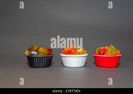 Colourful and small gel candies in small bowls. Grey ground and background. Stock Photo