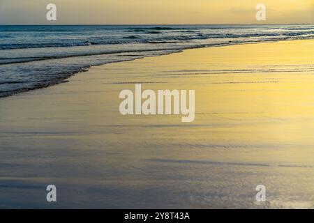 Golden light reflecting off the wet sand as gentle waves roll in. Stock Photo