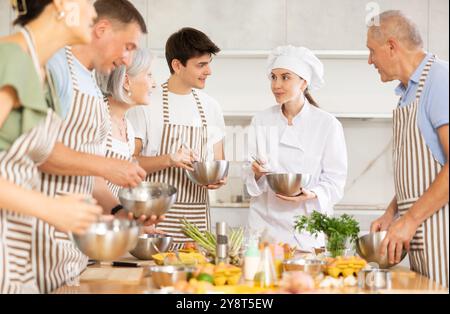 Female chef giving instructions to students standing around table in cooking class Stock Photo