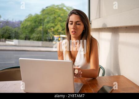 Worldwide work: Female developer working on laptop at restaurant. Woman freelancer is coding on computer at cafe. Caucasian lady is working remotely.  Stock Photo