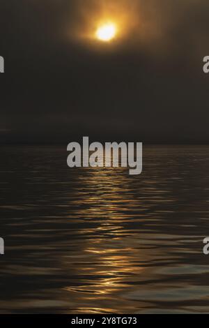 Sun breaking through clouds, reflection on slightly wavy sea surface, Woodfjord, Svalbard and Jan Mayen archipelago, Norway, Europe Stock Photo