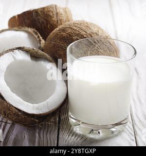 Drinking glass of milk or yogurt on blue napkin on white wooden table with coconut aside Stock Photo