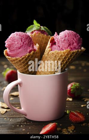Wafer cones with strawberry icecream in pink mug on wooden kitchen table Stock Photo
