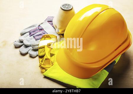 Yellow plastic hard hat, glasses, respirator and protective gloves laying on plywood. Safe labor concept Stock Photo