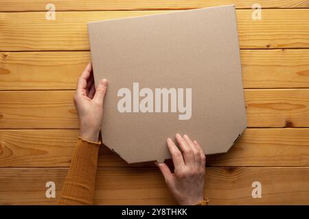 Pizza closed carton box in human caucasian hands on natural wooden table flat lay mockup with blank space Stock Photo