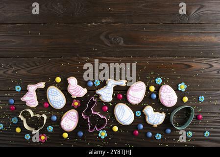 Cookie cutters and Easter frosted cookies in shape of egg, chicken and rabbit on dark wooden background. Flat lay with copy space Stock Photo