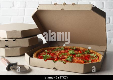 Large Pizza in open carton box and cutter on kitchen table closeup view Stock Photo