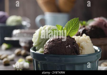 Three scoops of Vanilla pistachio and chocolate icecream balls in clay bowls on wooden kitchen table Stock Photo