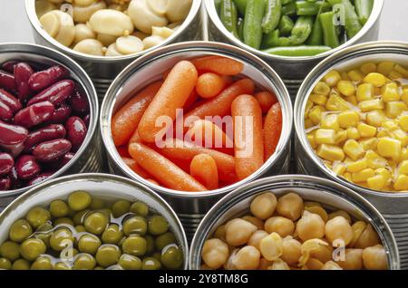 Canned vegetables in opened tin cans on kitchen table. Non-perishable long shelf life foods background Stock Photo