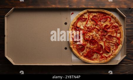 Pepperoni pizza with bell peppers in open carton box on dark wooden table flat lay with copy-space Stock Photo