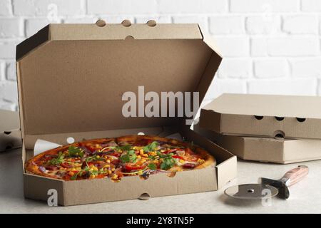 Large Pizza in open carton box and cutter on kitchen table closeup view Stock Photo