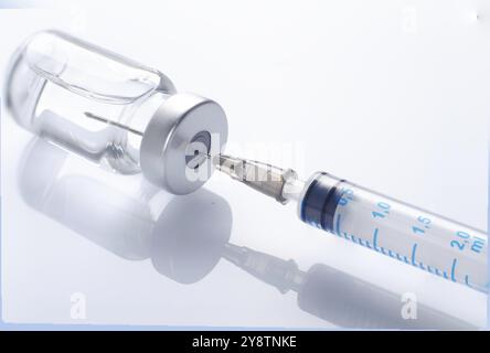 Just opened vaccine vial with inserted syringe for injection treatment on medical table. Vaccination or immunization care concept background Stock Photo