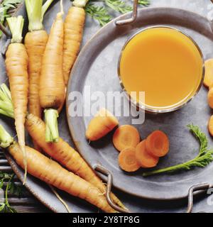 Vegetarian background of old fashioned tray with fresh organic carrots and juice on kitchen wooden table. Top view Stock Photo