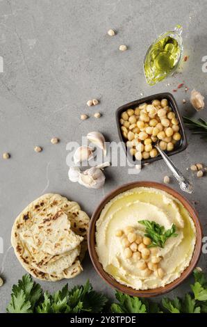 Hummus topped with chickpeas, olive oil and green coriander leaves on stone table with pita bread aside Stock Photo