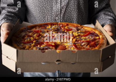 Caucasian male hands hold large open carton box with pepperoni pizza with sweetcorn front view Stock Photo