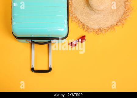 Turquoise suitcase, straw hat and sunglasses on yellow background, flat lay. Space for text Stock Photo