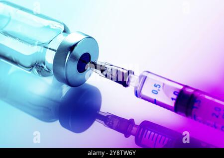 Just opened vaccine vial with inserted syringe for injection treatment on medical table. Vaccination or immunization care concept background Stock Photo